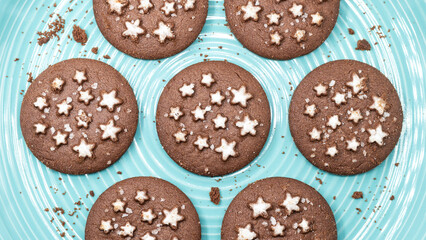 Close-up of cocoa and hazelnut biscuits decorated with sugar stars on turquoise plate, sweet...