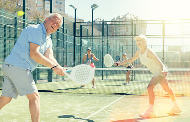 Determined sporty older husband and wife doing his best playing padel in court