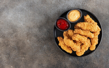 Crispy chicken breast strips with ketchup and cheese sause on a dark background. Top view. Copy space. Fast food