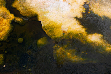 Stunning geothermal hot spring creates abstract natural art with vibrant yellow and dark water, showcasing unique geological formations and textures