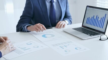 Business colleagues discussing financial data on a laptop and printed documents while analyzing charts and market trends. Business people and finance concept - Powered by Adobe