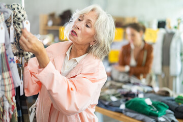 Elderly woman chooses a scarf and stole for the winter with interest, she pays attention to the...