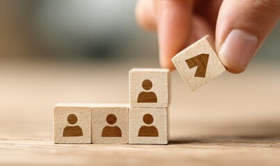 A hand places a wooden block with an upward arrow symbol on top of a step-like arrangement of wooden blocks, each block having a person icon