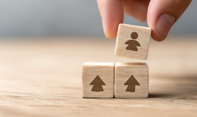 A hand places a small wooden block with a person icon on top of two other blocks with upward-pointing arrows