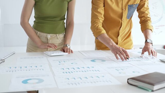 Business professionals analyzing financial reports, pointing at charts during collaborative meeting, discussing data with focused professional demeanor