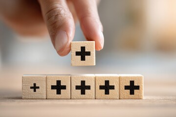 A hand places a small wooden block with a plus sign on top of other blocks