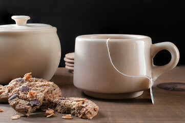 Cup of tea with oatmeal cookies and sugar bowl on black background, side view
