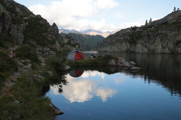 Obraz na płótnie Canvas Escape to breathtaking alpine lake camping with your dog and a red tent reflecting in the water for an unforgettable adventure