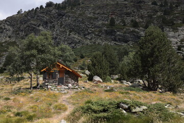 Rustic stone cabin nestled in a wildflower meadow at the base of a rugged mountain, evoking...