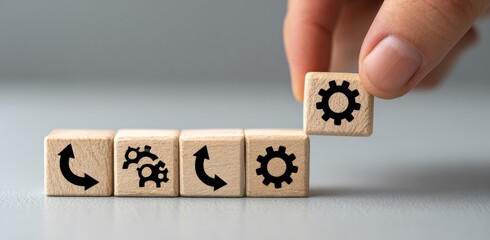 Wooden blocks with gear and arrow icons, arranged in a row, with one block being lifted by a hand