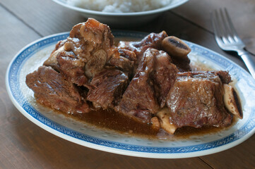 Plato con costillas de res con salsa de ostion, platillo asiato, oriental, sobre una mesa rustica de madera, con un tenedor al lado.