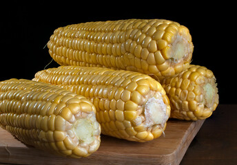 Naturaleza muerta o bodegon fotografico. Elotes amarillos sobre una tabla de cortar de madera con fondo negro, fotografia de acercamiento o macro fotografia