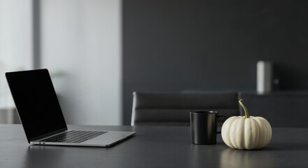 A sleek silver laptop with a blank dark screen sits on a modern grey desk, accompanied by a black coffee mug and a small white decorative pumpkin.