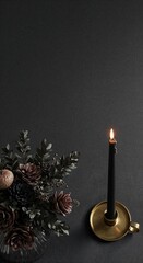 A top-down view of a lit black taper candle in a brass holder next to a decorative bouquet of dried flowers and pinecones on a dark textured surface.