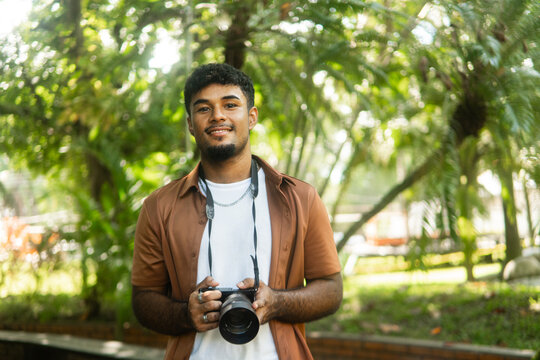 Young man holding camera smiling outdoors in park