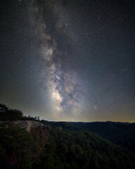 Bright stars and the stunning Milky Way stretch across a clear night sky above a dense forest. This breathtaking view captures the beauty of the universe at night. Auxier Ridge. Red River Gorge.
