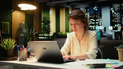 Woman in a dark office after hours leaning back in her office chair, meditating in a calm casual state. Relaxed pose and empowered expression reflect fulfillment of career goals. Camera A.