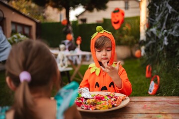Little girl wearing pumpkin costume choosing candies at Halloween party in the garden
