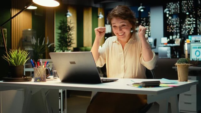 Delighted excited employee reading good news from notification late at night, celebrating a career breakthrough and awesome opportunity in the office. Proud businesswoman beaming. Camera A.