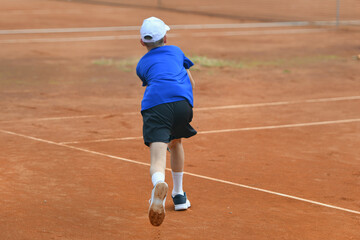 Young boy playing tennis on real court outdoor