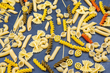 Diverse array of uncooked pasta varieties on dark background showcasing textures and shapes