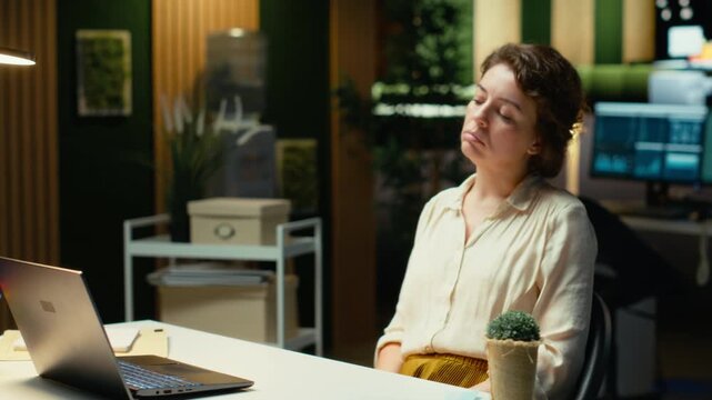 Entrepreneur contemplating on a complex problem in a dark office late at night, strategizing and typing options on laptop. Seeking a logical solution through careful concentration. Camera B.