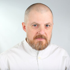 Man with a beard and shaved head poses against a neutral backdrop in a professional setting