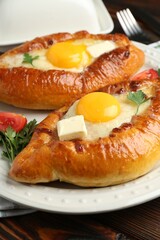 Tasty khachapuri with cheese and eggs served on wooden table, closeup