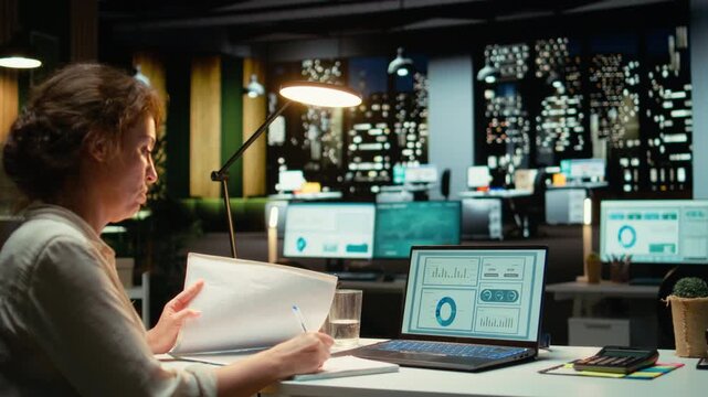 Executive is proofreading a report and documenting updates at night time in the strategy room, researching numbers to create a compelling presentation for next meeting, growth plan. Camera A.