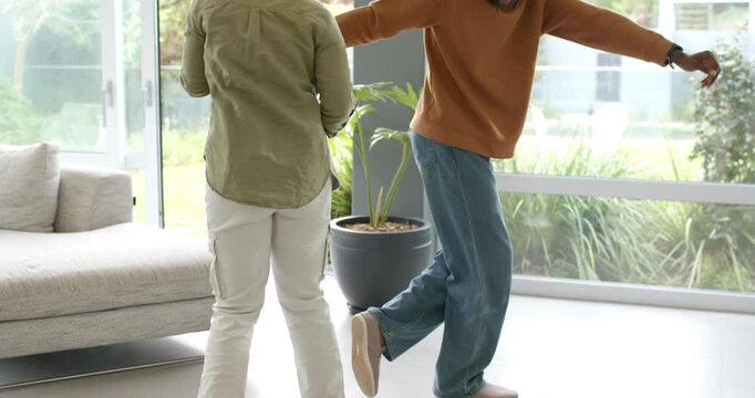 African American couple practicing dance steps, arms extended by sliding glass doors in living room