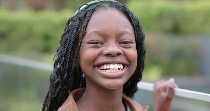 African American girl leaning on railing by canal giggling and brushing drifting leaf from ribbon