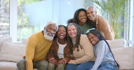 Photographer calling extended family gathering on sofa, leaning inward and laughing for portrait