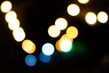 Foto abstrak bokeh cahaya berwarna kuning, putih, biru, dan hijau di malam hari dengan latar belakang hitam. Cahaya yang tidak fokus menciptakan efek artistik dan atmosfer estetik yang cocok digunakan