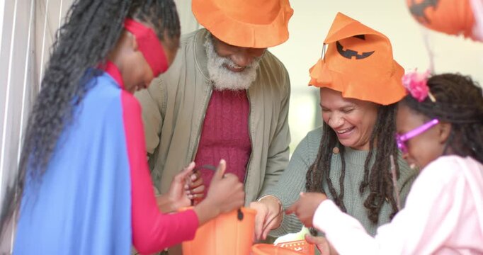Diverse family filling Halloween buckets at entryway after superhero girl reaching into candy bowl
