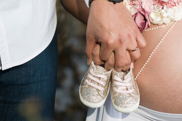 Pareja heterosexual, sosteniendo zapatos e bebe en se&ntilde;al de que la mujer esta embarazada y mostrando parte de su panza con su bebe