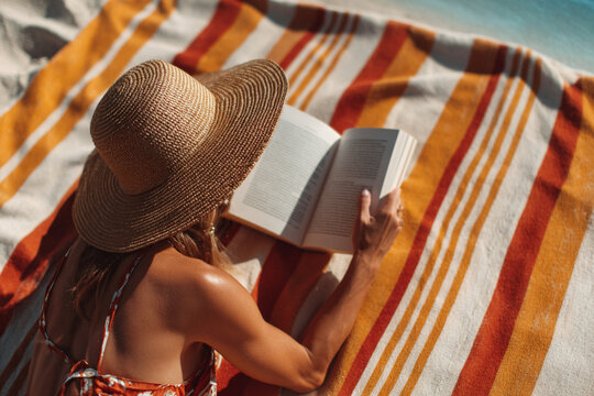 Woman relaxing on beach reading book on striped towel during sunny day
