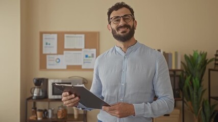 Hispanic man with beard holding clipboard stands in modern office with charts in background showcasing professional indoor setting with relaxed demeanor. - Powered by Adobe