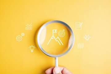 Mission target and goal achievement with magnifying glass on mountain peak and flag, vision, strategy, planning, business success, and accomplishment.