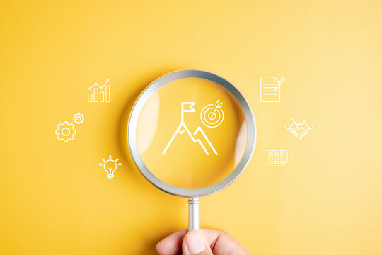 Mission target and goal achievement with magnifying glass on mountain peak and flag, vision, strategy, planning, business success, and accomplishment.