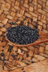 Black sesame seeds in wooden spoon on bamboo mat - organic healthy cooking ingredient