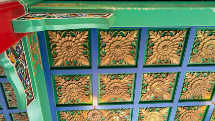 View upwards at a wooden pavilion roof with a repeating tile pattern and painted vibrant shades of gold, green, blue and red. 