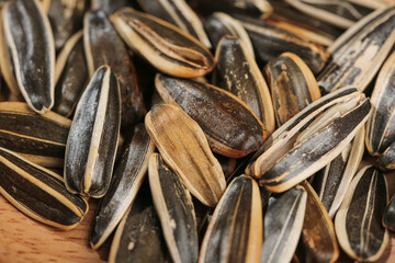 Black striped sunflower seeds with natural shells on wooden background - healthy snack and cooking ingredient