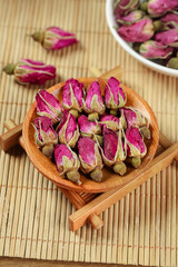 Dried Rose Buds in Wooden Bowl for Herbal Tea and Wellness on Bamboo Mat