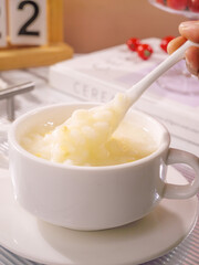 Fresh corn soup with spoon in white ceramic cup, healthy homemade meal preparation in kitchen