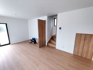 新築住宅の広々としたリビングダイニングの様子を捉えた写真白い壁と明るい木目のフローリングが特徴で木製のドアと階段があるシンプルな内装