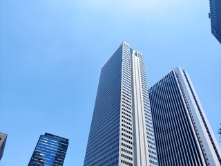 快晴の青空を背景に東京都新宿区の超高層ビル群を下から見上げるように捉えた写真無機質で巨大な現代建築の構造が強調されている