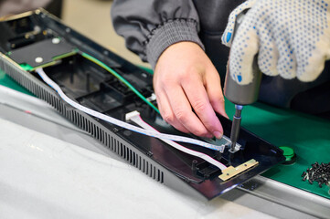 Technician assembling electronic device in factory during daytime with tools focused on intricate...
