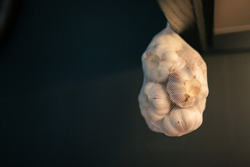 Bag full of garlic hanging in black kitchen with copy space