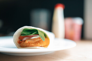 Plated chicken wrap on kitchen bench with tomato, spinach and kimchi