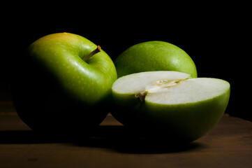 Arte fotografico o bodegon estilo barroco renacentista con tecnica claroscuro. Manzanas verdes sobre mesa de madera con fondo negro vista frontal.
